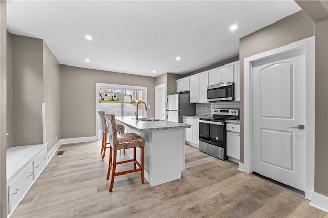 kitchen featuring appliances with stainless steel finishes, white cabinets, a kitchen bar, a kitchen island with sink, and sink