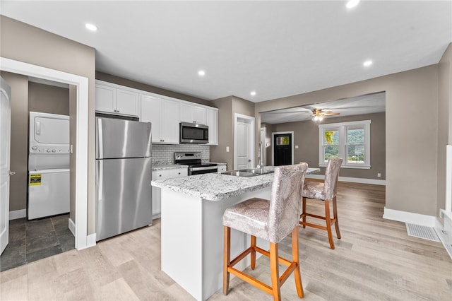 kitchen featuring white cabinetry, an island with sink, a breakfast bar, stainless steel appliances, and stacked washer / drying machine