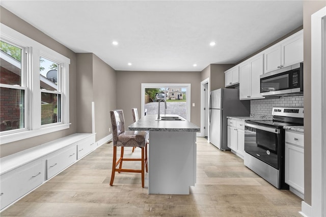 kitchen featuring a healthy amount of sunlight, white cabinets, appliances with stainless steel finishes, and a kitchen island with sink