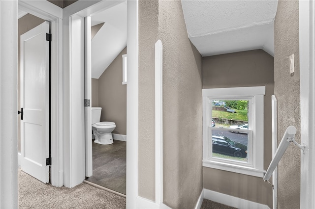 hall featuring a textured ceiling, vaulted ceiling, and light colored carpet