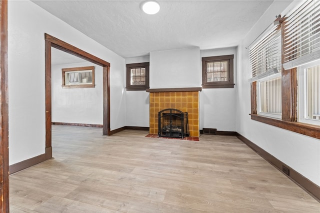 unfurnished living room featuring a fireplace, light hardwood / wood-style floors, a textured ceiling, and plenty of natural light