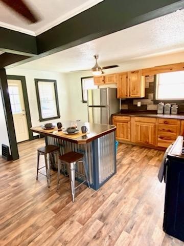 kitchen featuring ceiling fan, a kitchen breakfast bar, stainless steel refrigerator, electric stove, and light hardwood / wood-style floors