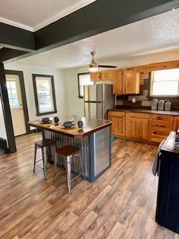 kitchen with hardwood / wood-style flooring, black range with electric cooktop, stainless steel fridge, a kitchen bar, and ceiling fan