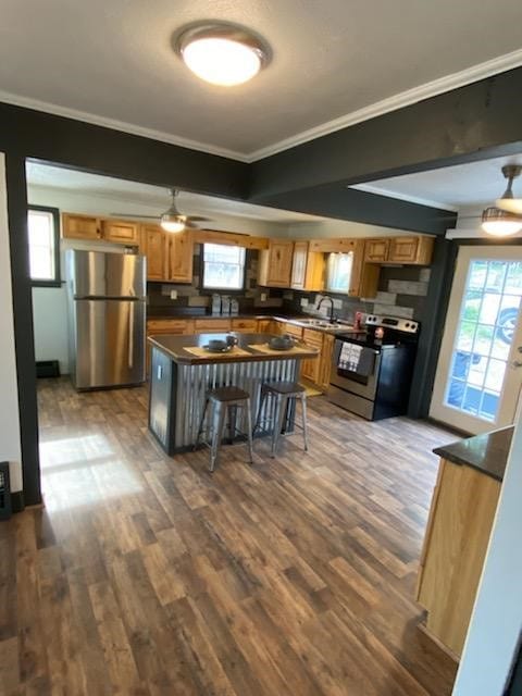 kitchen with a kitchen island, stainless steel appliances, ornamental molding, a breakfast bar, and dark hardwood / wood-style flooring