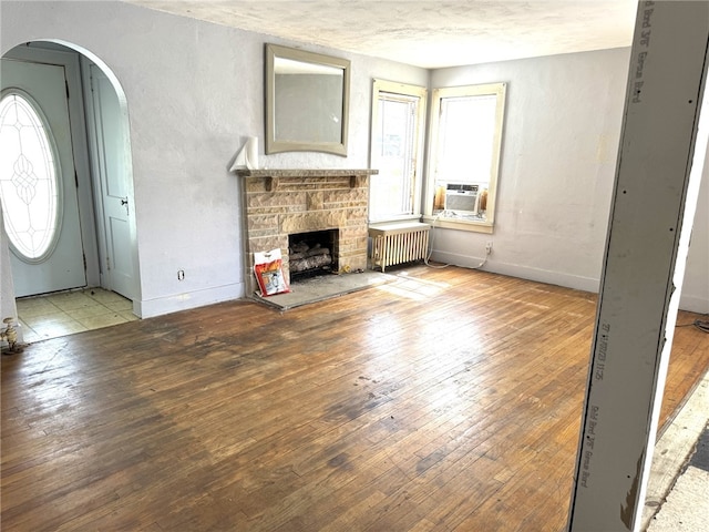 unfurnished living room featuring cooling unit, a fireplace, light hardwood / wood-style floors, and radiator heating unit