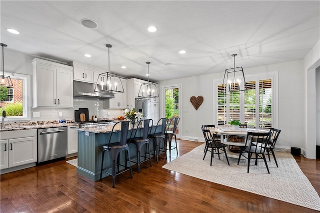 kitchen featuring pendant lighting, a center island, white cabinetry, light stone countertops, and stainless steel dishwasher