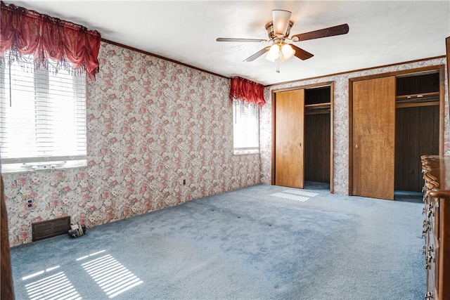 unfurnished bedroom featuring carpet, two closets, ceiling fan, and crown molding