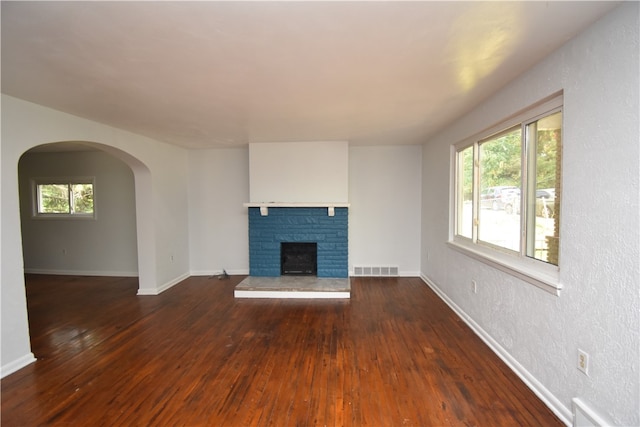 unfurnished living room with a stone fireplace, dark hardwood / wood-style flooring, and a healthy amount of sunlight