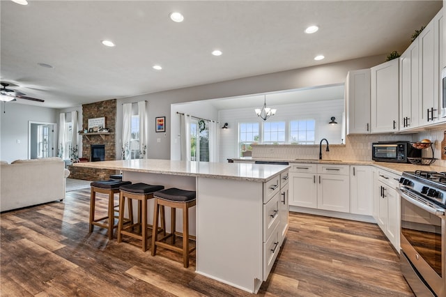 kitchen featuring white cabinets, ceiling fan with notable chandelier, a fireplace, dark hardwood / wood-style flooring, and gas stove