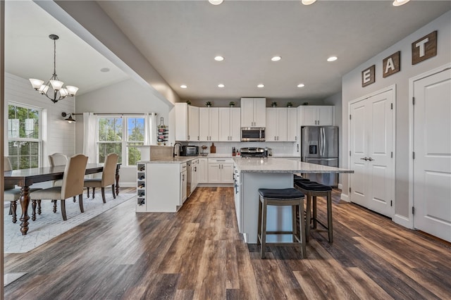 kitchen with pendant lighting, white cabinetry, vaulted ceiling, appliances with stainless steel finishes, and dark hardwood / wood-style flooring