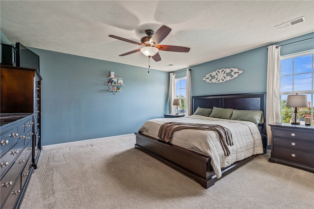 bedroom featuring multiple windows, light colored carpet, ceiling fan, and a textured ceiling