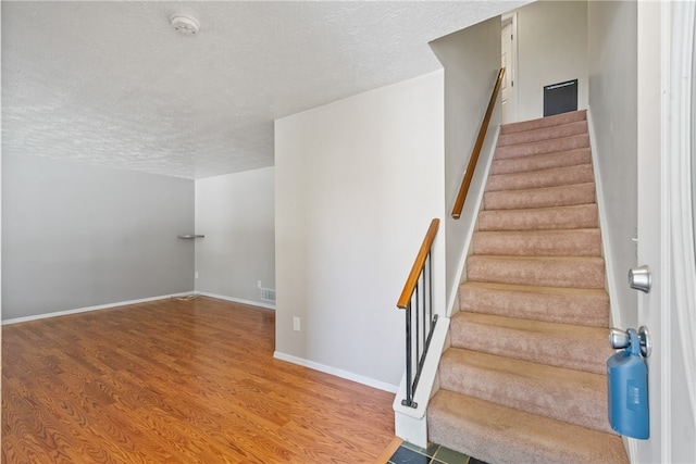 stairs featuring a textured ceiling and hardwood / wood-style floors