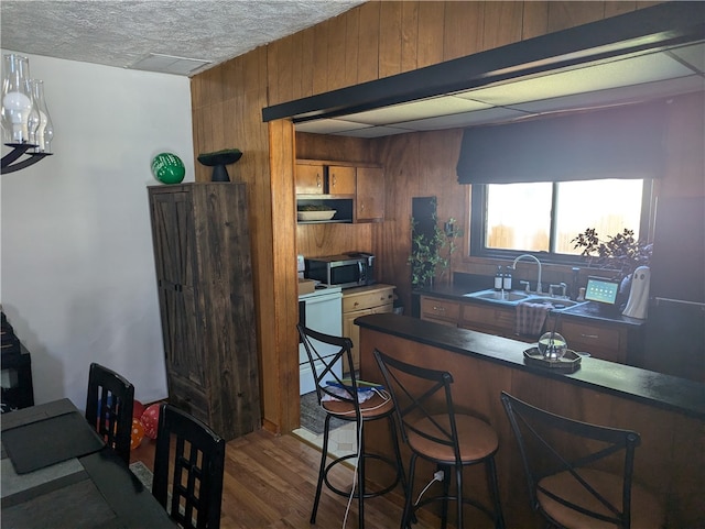 interior space featuring white stove, a kitchen bar, wooden walls, dark hardwood / wood-style floors, and sink