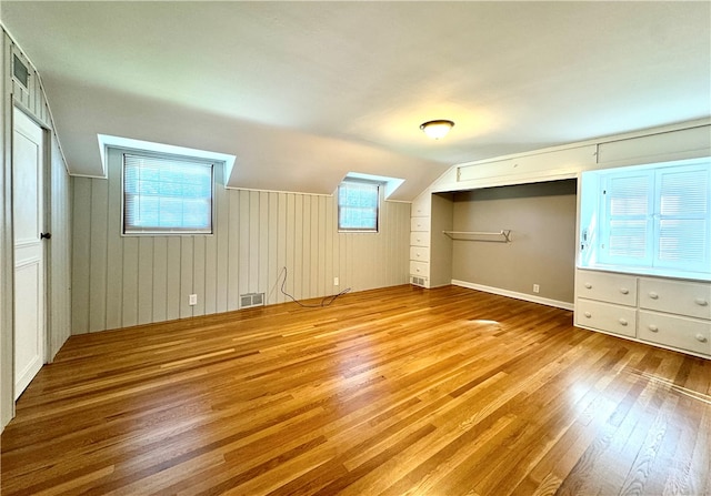 bonus room with light hardwood / wood-style floors, lofted ceiling, a wealth of natural light, and wooden walls