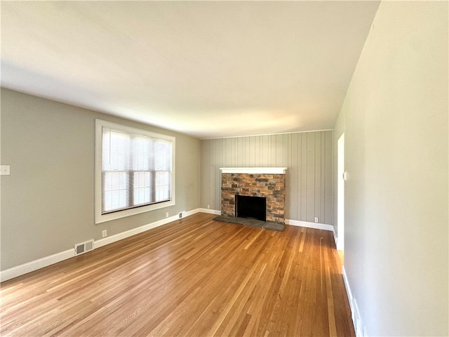 unfurnished living room featuring light hardwood / wood-style floors, wood walls, and a fireplace