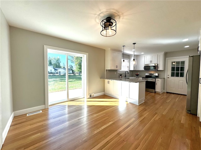 kitchen with appliances with stainless steel finishes, kitchen peninsula, white cabinetry, and light hardwood / wood-style floors