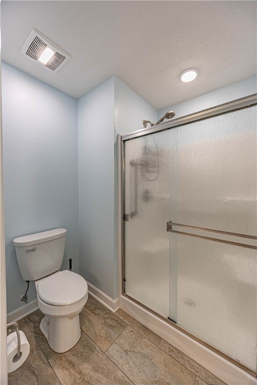 bathroom with a textured ceiling, a shower with door, and toilet