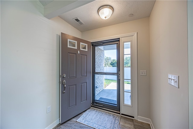 foyer entrance featuring vaulted ceiling with beams, a textured ceiling, and a healthy amount of sunlight