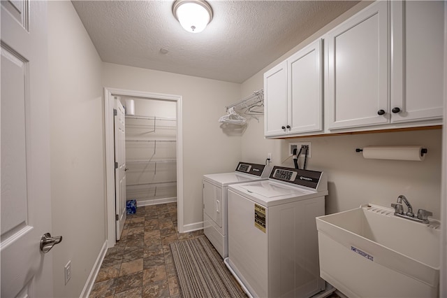 clothes washing area with cabinets, a textured ceiling, washer and dryer, and sink