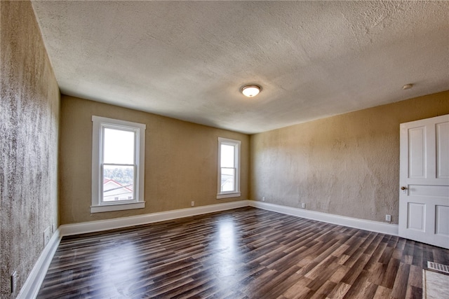 empty room with a textured ceiling, dark wood-type flooring, and a wealth of natural light