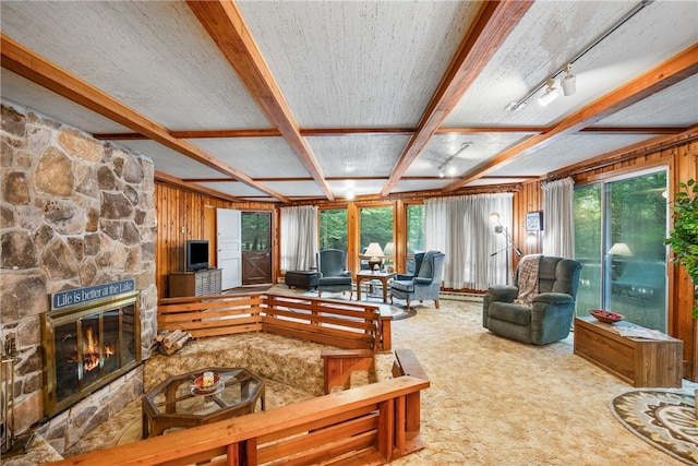 living room with carpet flooring, a textured ceiling, a stone fireplace, and wooden walls