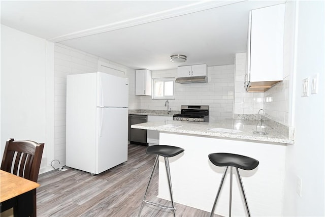 kitchen featuring kitchen peninsula, appliances with stainless steel finishes, light wood-type flooring, white cabinets, and a breakfast bar area