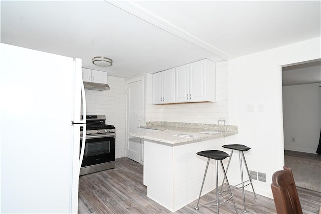 kitchen with white refrigerator, kitchen peninsula, range hood, stainless steel range oven, and white cabinetry