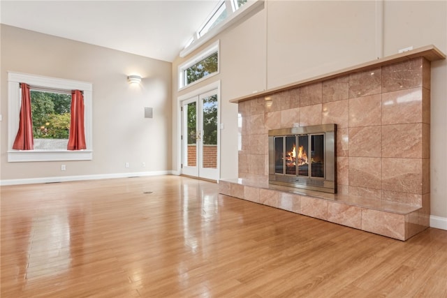 unfurnished living room with light wood-type flooring, plenty of natural light, lofted ceiling, and a tile fireplace