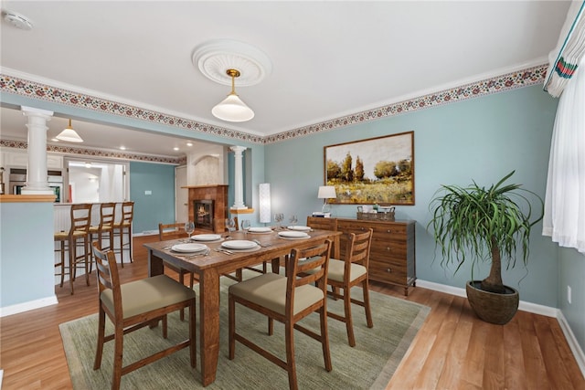 dining space featuring ornate columns, hardwood / wood-style floors, crown molding, and a high end fireplace