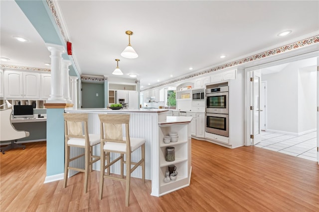 kitchen featuring white cabinetry, decorative columns, built in desk, and light hardwood / wood-style flooring