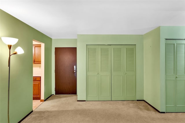 unfurnished bedroom with multiple closets, light colored carpet, and ensuite bathroom