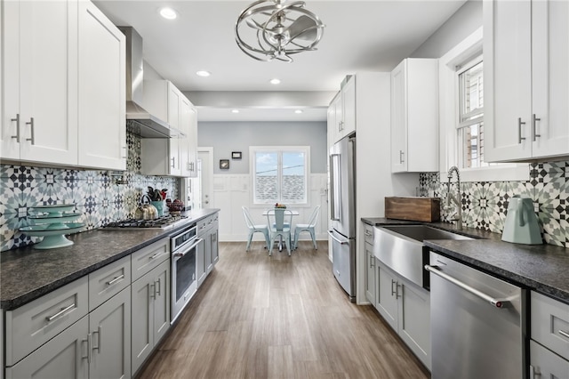 kitchen with pendant lighting, white cabinetry, wall chimney range hood, stainless steel appliances, and hardwood / wood-style floors