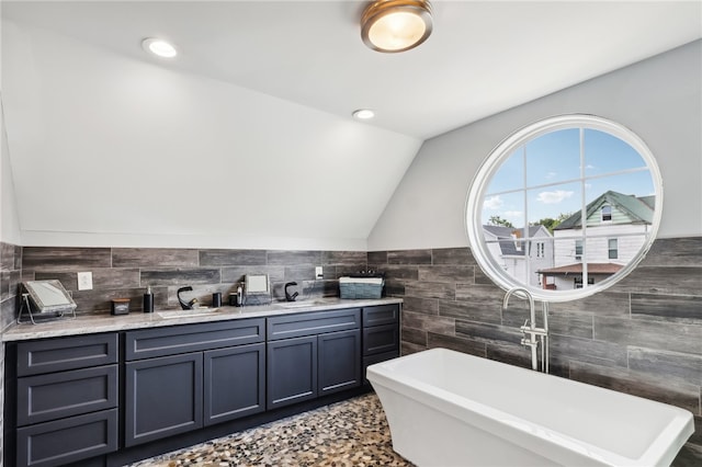 bathroom with tile walls, lofted ceiling, a tub to relax in, and vanity