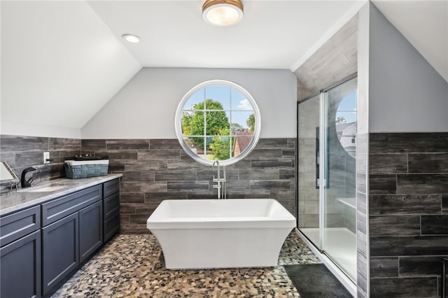 bathroom with tile walls, vaulted ceiling, vanity, and shower with separate bathtub