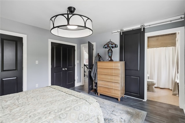 bedroom featuring a barn door, ensuite bath, and dark hardwood / wood-style flooring