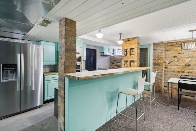 kitchen featuring a kitchen bar, butcher block countertops, stainless steel appliances, and brick wall