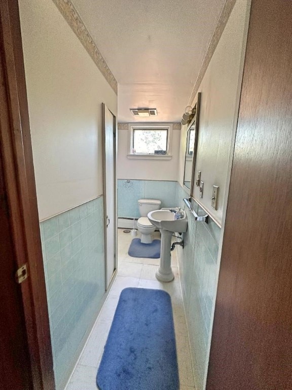 bathroom featuring a bidet, a shower with shower door, a baseboard heating unit, tile walls, and toilet