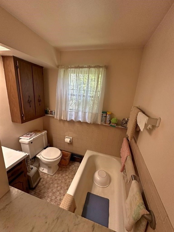 bathroom with tile walls, a textured ceiling, a tub, vanity, and toilet