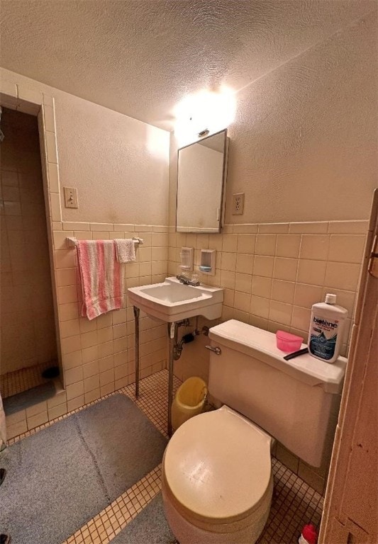 bathroom featuring toilet, sink, a textured ceiling, tile walls, and tile patterned flooring