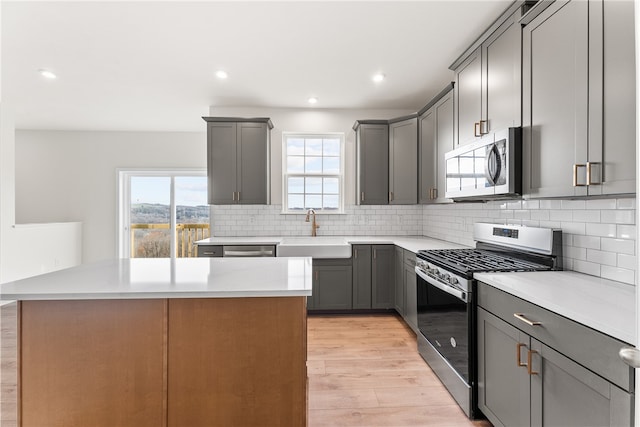 kitchen with gray cabinetry, sink, light hardwood / wood-style floors, a kitchen island, and appliances with stainless steel finishes