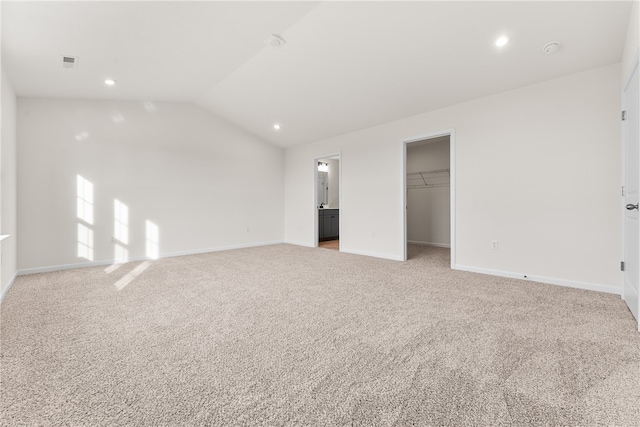 unfurnished bedroom with ensuite bath, a spacious closet, vaulted ceiling, light carpet, and a closet