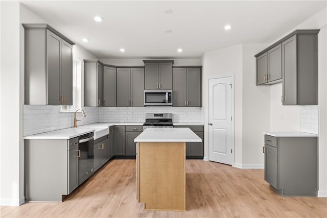 kitchen with gray cabinets, a kitchen island, stainless steel appliances, and light wood-type flooring