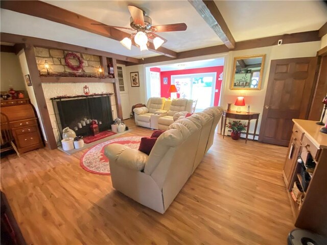 living room with a tile fireplace, beam ceiling, light wood-type flooring, and ceiling fan