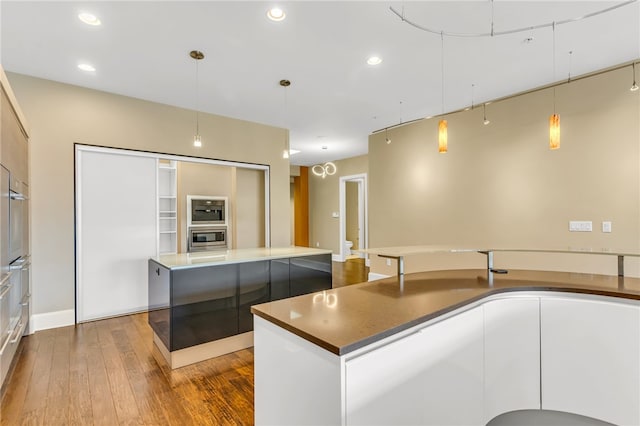 kitchen with hanging light fixtures, white cabinetry, wood-type flooring, and an island with sink