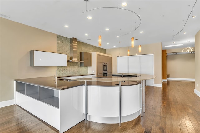 kitchen with hanging light fixtures, hardwood / wood-style floors, wall chimney range hood, and white cabinets