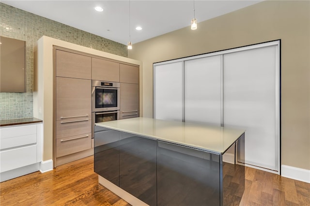 kitchen featuring decorative backsplash, light hardwood / wood-style floors, hanging light fixtures, and stainless steel double oven