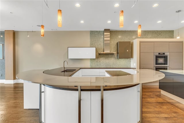 kitchen featuring hanging light fixtures, sink, wall chimney exhaust hood, dark wood-type flooring, and stainless steel double oven