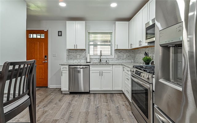 kitchen with appliances with stainless steel finishes, light stone counters, white cabinets, light hardwood / wood-style flooring, and sink