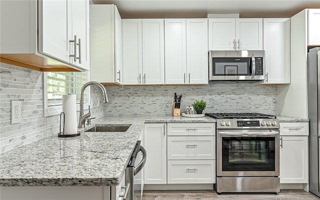 kitchen with light stone counters, stainless steel appliances, sink, and white cabinetry