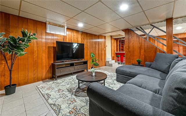 living room featuring a drop ceiling, wooden walls, and tile patterned floors